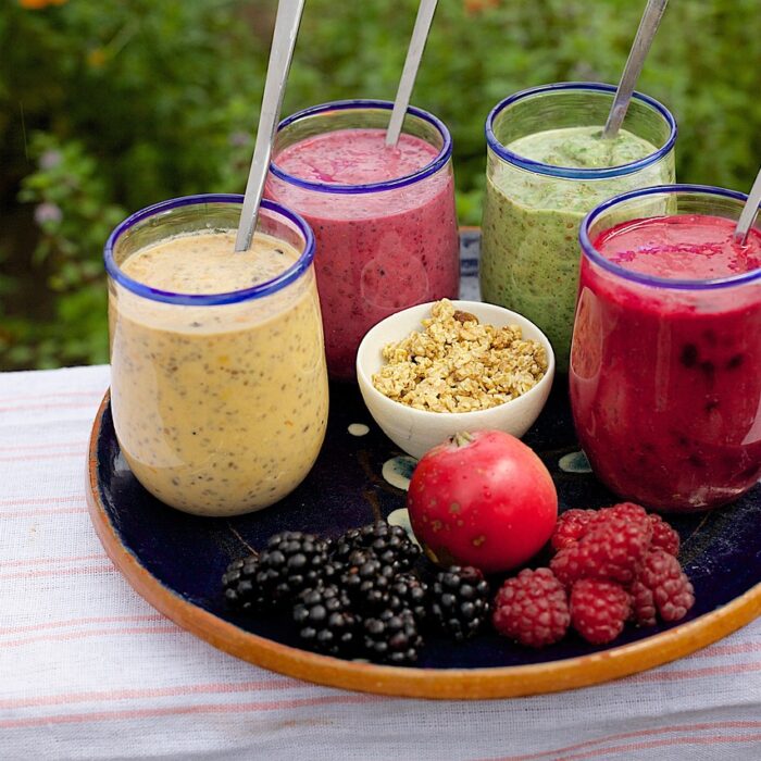 An assortment of smoothies on a tray, surrounded by fresh fruit.