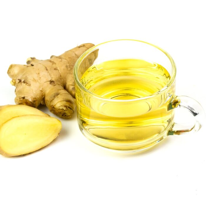 A ginger piece snapped in two next to a hot cup of ginger tea in a glass tumbler