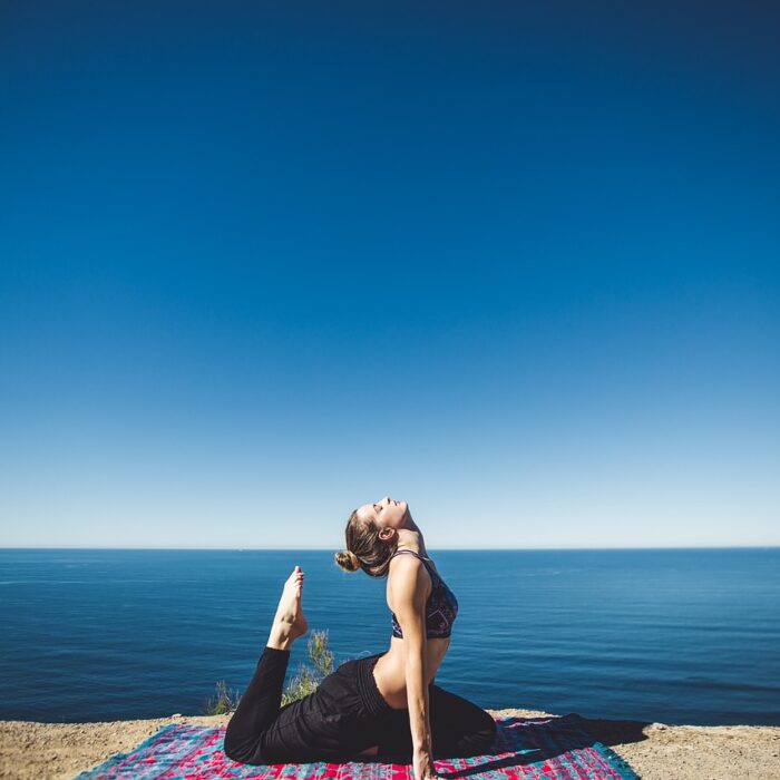 A woman stretching on a mat with the ocean in the background.